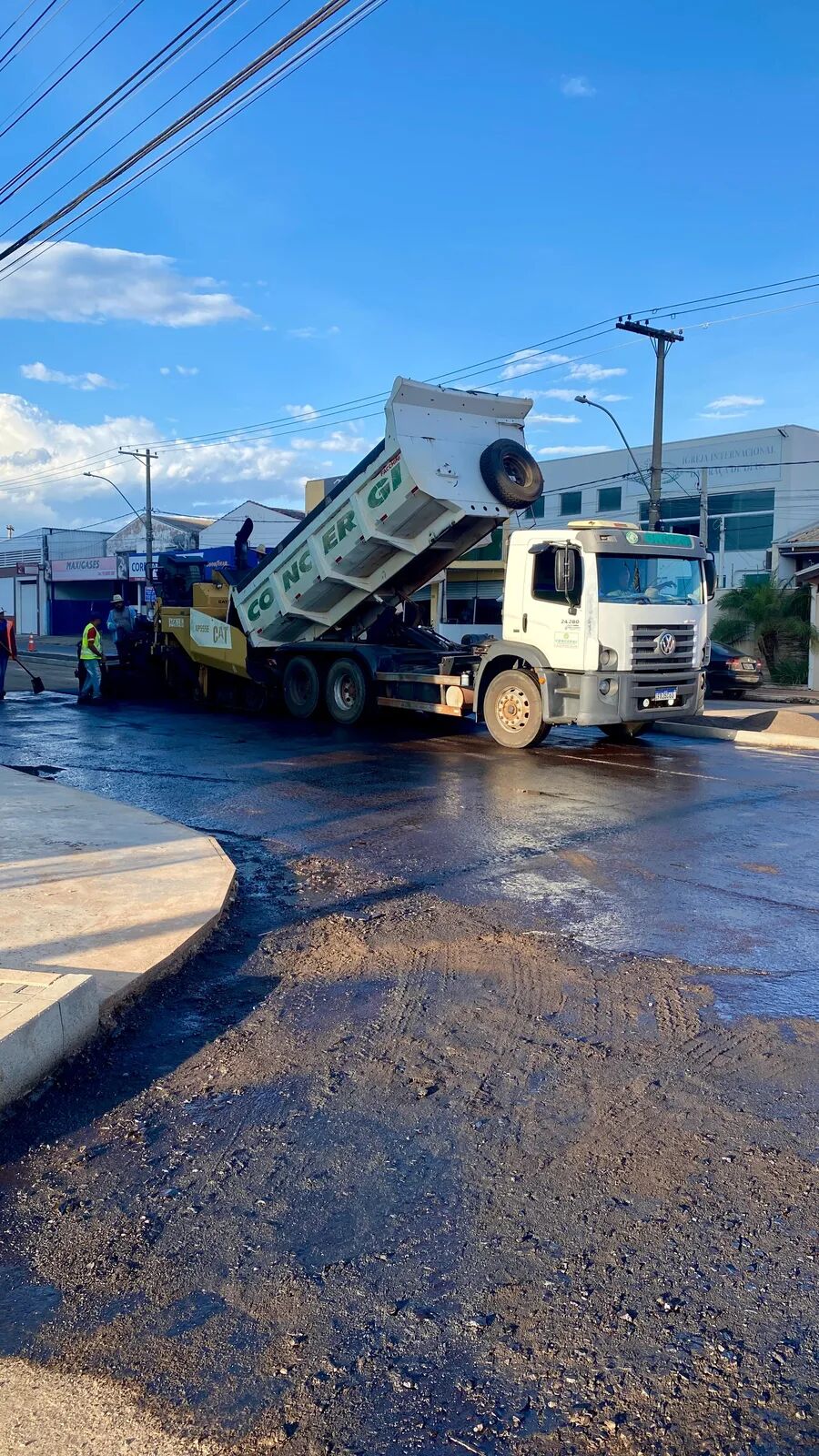 Caminhão VW CONCERGI descarregando CBUQ na vibroacabadora em operação urbana de pavimentação