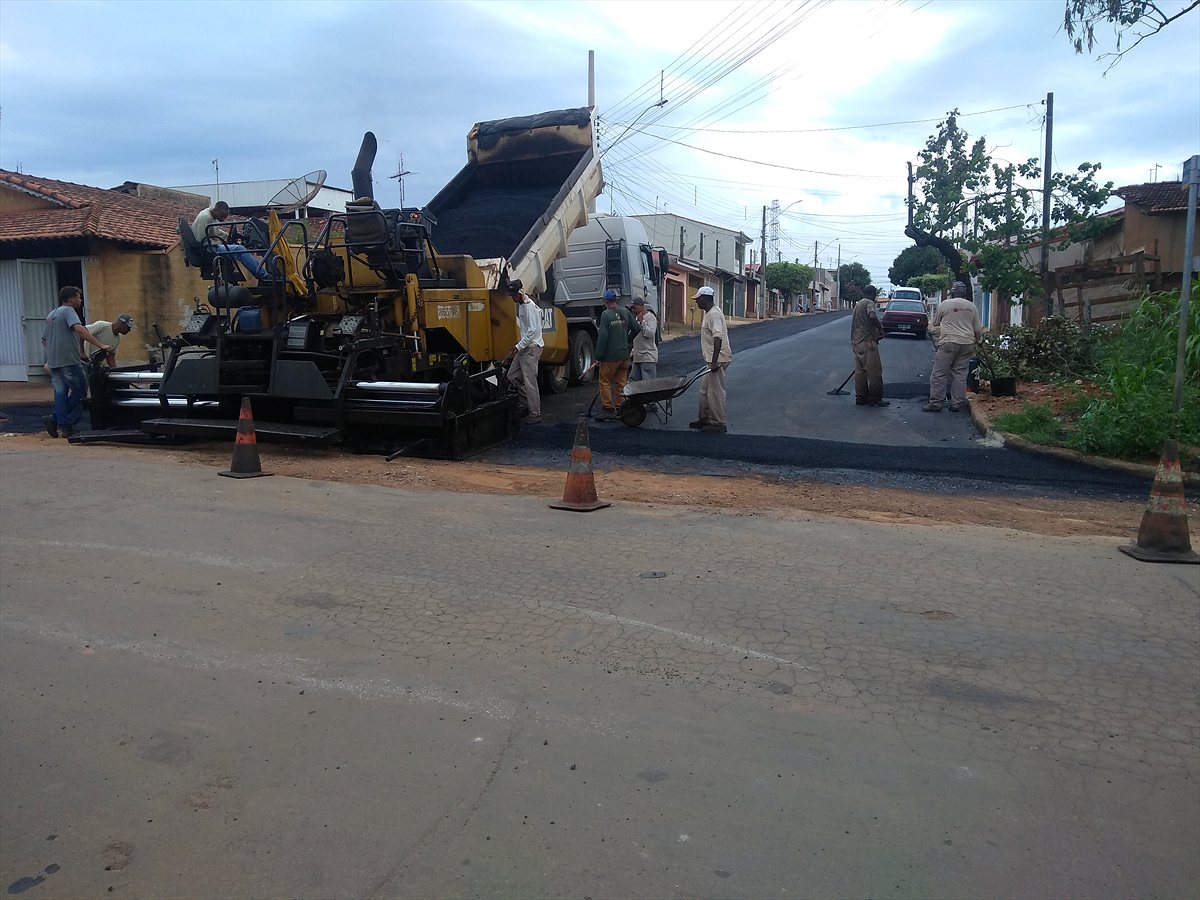 Vibroacabadora e caminhão basculante aplicando CBUQ em rua urbana, com equipe e sinalização de obra