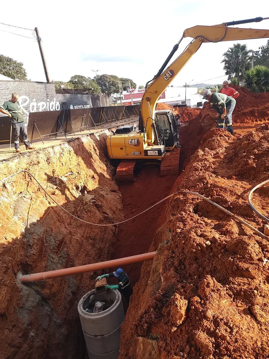 Escavadeira hidráulica em vala urbana com poço de visita