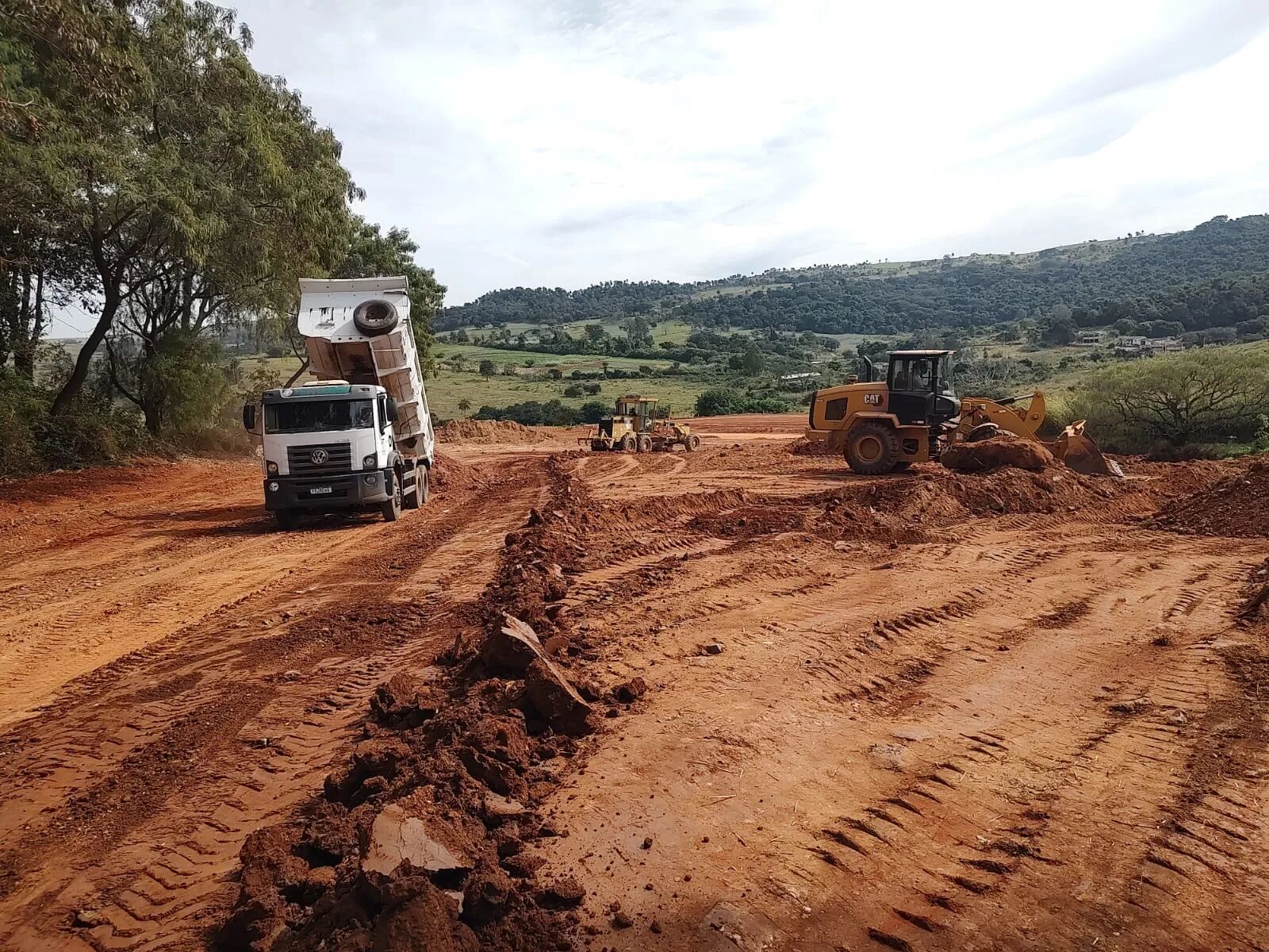 Frota CONCERGI em operação de terraplanagem: caminhão basculante, motoniveladora e pá-carregadeira